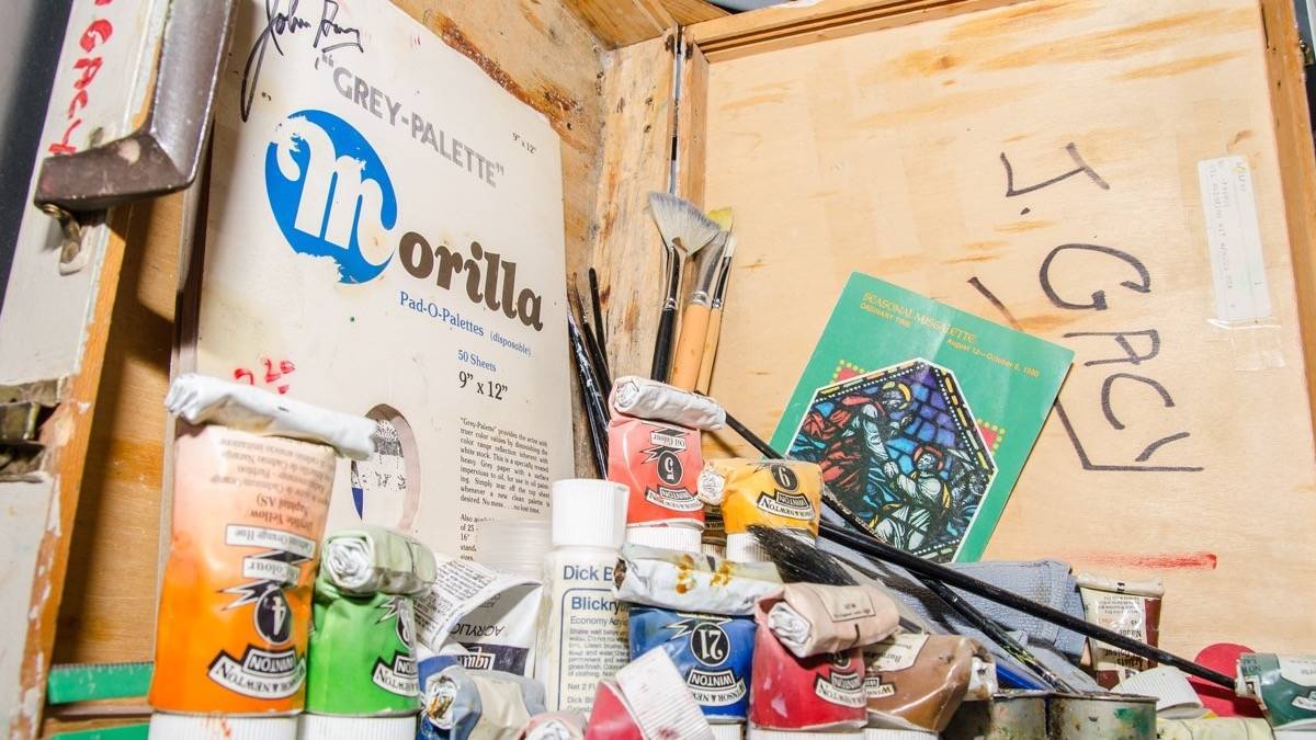 Paint, brushes, and a sketch pad in a wooden box with J Gacy written on the boxy